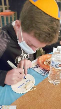Noah Reich of Highland Mills writes a message of hope for sick children at Chabad’s CTeen giving event “Tiles for Smiles” with Rabbi Pesach and Chana Burston of Chabad of Orange County.