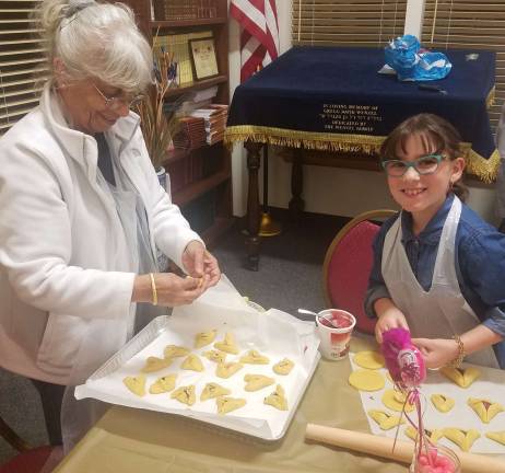Rivkah Burston, age 9 and daughter of Rabbi Pesach and Chana Burston, shows Samira Galler of Monroe how to shape a Hamantashen cookie.