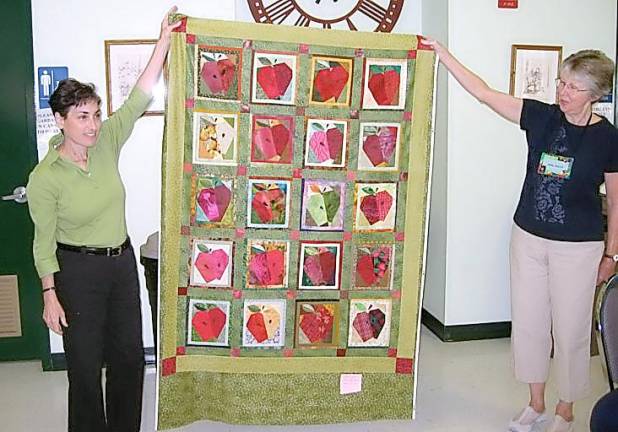 Louise LoPinto Hutchison and Anne Sigler hold the Warwick Valley Quilters’ Guild’s Applefest quilt top with blocks designed by Hutchison and made by guild members in 2008.