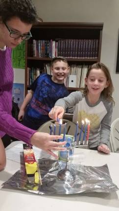 Chabad Hebrew School student Layla Sale of Central Valley learns how to light the menorah, with the assistance of teacher Freidi Holtzberg, as Matthew Graves looks on.