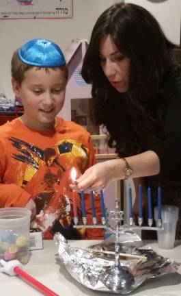Chana Burston teaches Chabad Hebrew School student Andrew Redling of Monroe how to safely light the traditional Hanukkah menorah.