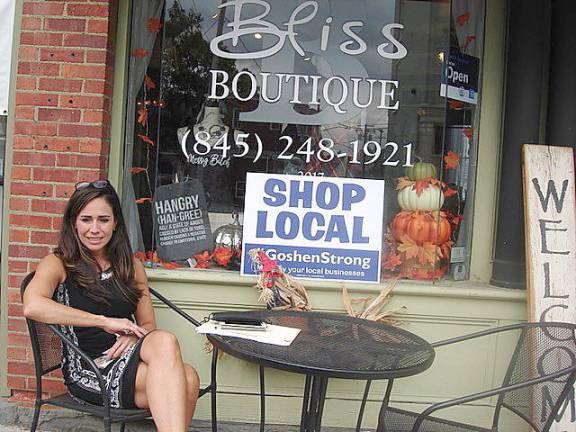 Sandra Fuentes, the owner of Bliss Boutique with her husband David, relaxes outside her shop on West Main Street in the Village of Goshen. Their shop carries “something for everyone,” said Fuentes. The WELCOME sign says it all: Come in and browse. Photo by Geri Corey.