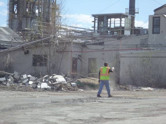 A worker with a facemask at the former Nepera chemical plant in Harriman directs a truck while standing in front of a pile of rubble as demolition work continues at the site. Photo by Nathan Mayberg