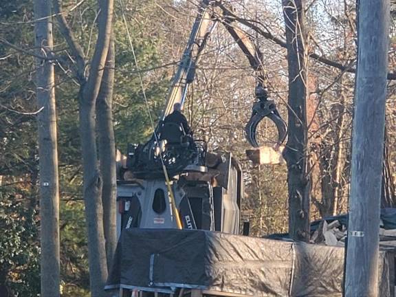 The logging truck’s crane carries a log off the load.