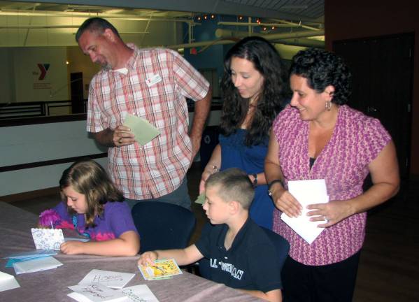 Monroe resident Gabrielle Schnaars, the&#160;granddaughter of Joan Smith, whose memory is honored through the organization Joan's Monarch Wishes,&#160;finishes signing a card&#160;to be sent&#160;to an&#160;oncology patient at Orange Regional Medical Center as her brother Charles Schnaars gets ready to hand her another card. &#160;Watching her and preparing for the July 27 greeting card signing evening at the South Orange Family YMCA are Jimmy&#160;Madison, the Y's associate program director, left, Jen Schnaars and&#160;Madiam Namdar, who is helping to coordinate the July 27 event. - photo by Nancy Kriz