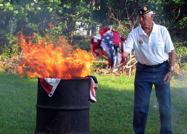 Jim Culligan keeps a safe distance from the fire as he tosses flags into the flames.
