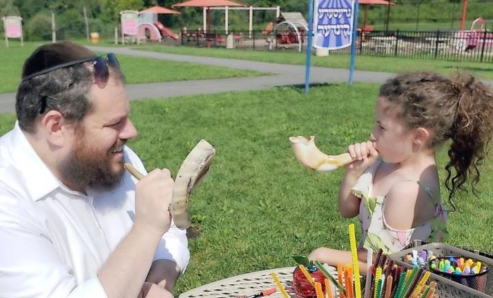 Rabbi Pesach Burston teaches Sofia Greenberg of Goshen, 8, how to sound the Shofar during a “Pre-High Holiday in the Park” event.