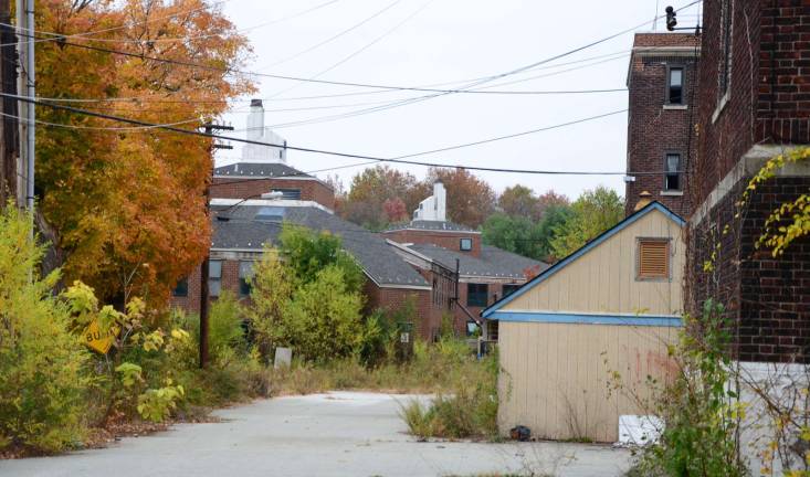 A maintenance shed at right and twin barracks crowned by smokestacks at center along a pitted road behind Camp LaGuardia's Main Building. Courtesy of Robert Yasinsac / Hudson Valley Ruins.