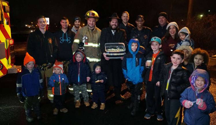 Photos Courtesy of Chabad of Orange County Rabbi Pesach Burston, director of Chabad of Orange County, holding a box full of chocolate coins to be dropped from a firetruck, pictured with members of the Monroe Fire Department and community members, at last year&#x2019;s event.This year&#x2019;s Menorah Lighting and Fire Truck Gelt Drop in Monroe takes place Tuesday, Dec. 12.