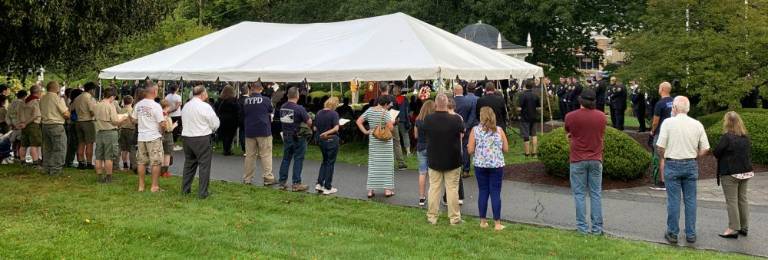 People gathered under the tent and along the lawn to observe the remembrance service.