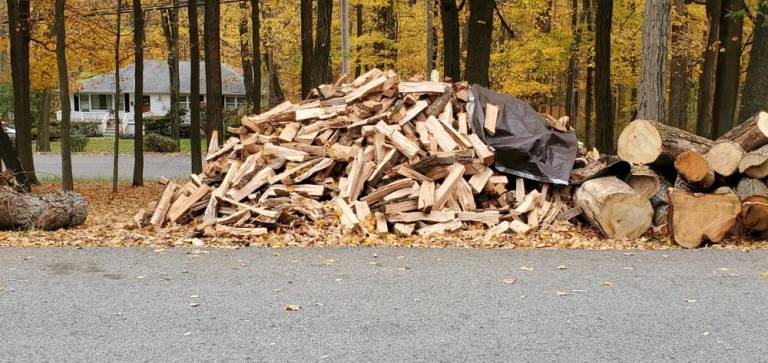 Piles of logs and cut wood abut the residential street.