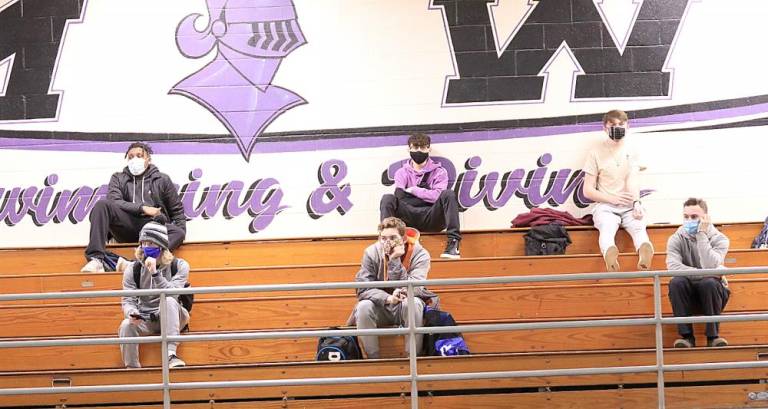 Boys from the swim and dive team remain masked and socially distant as they listen to the coach.